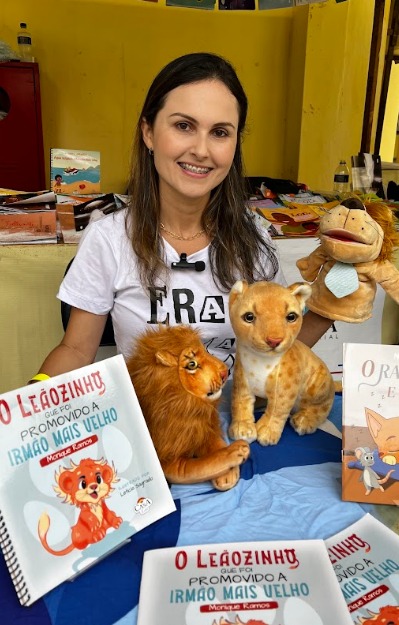 Autora com livros infantis e personagens durante a feira literária inclusiva do Instituto Benjamin Constant
